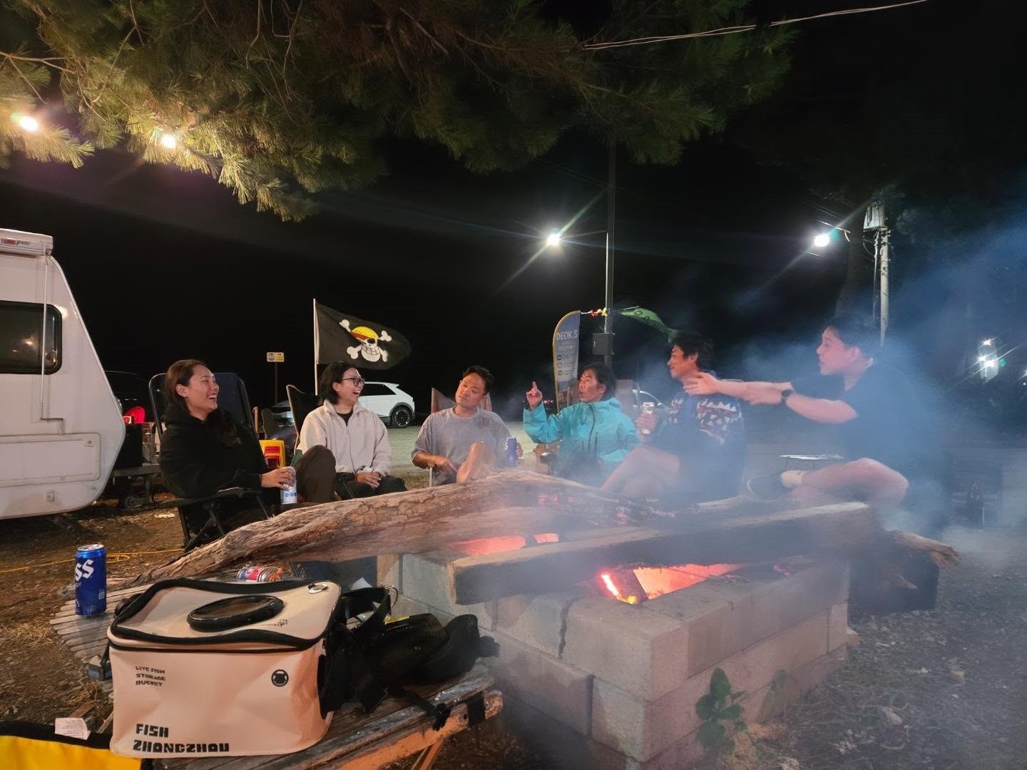 The group sitting in camping chairs around a fire at night