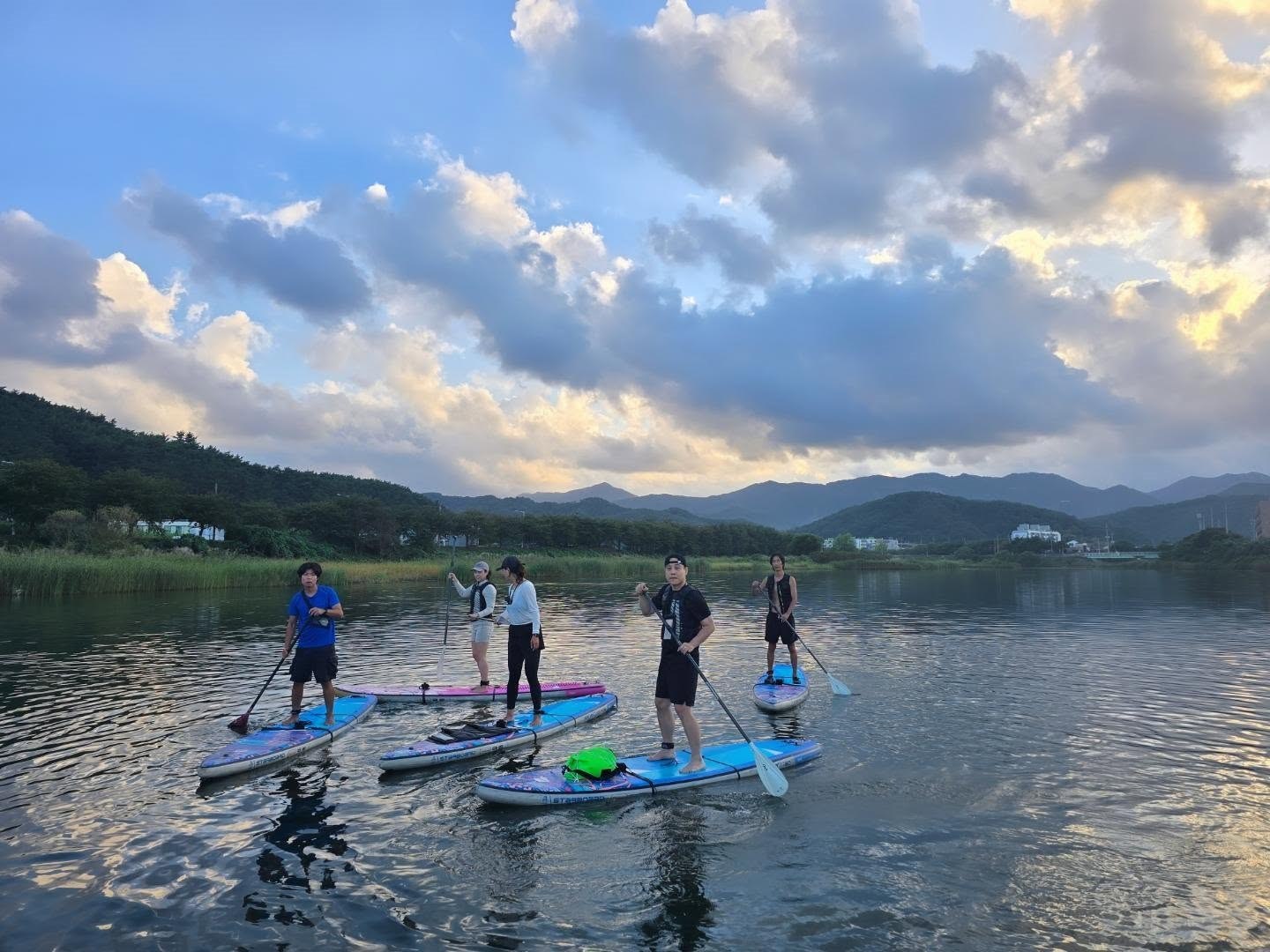Lunaru tour paddlers standing together on calm water beneath clouds and mountain ridges