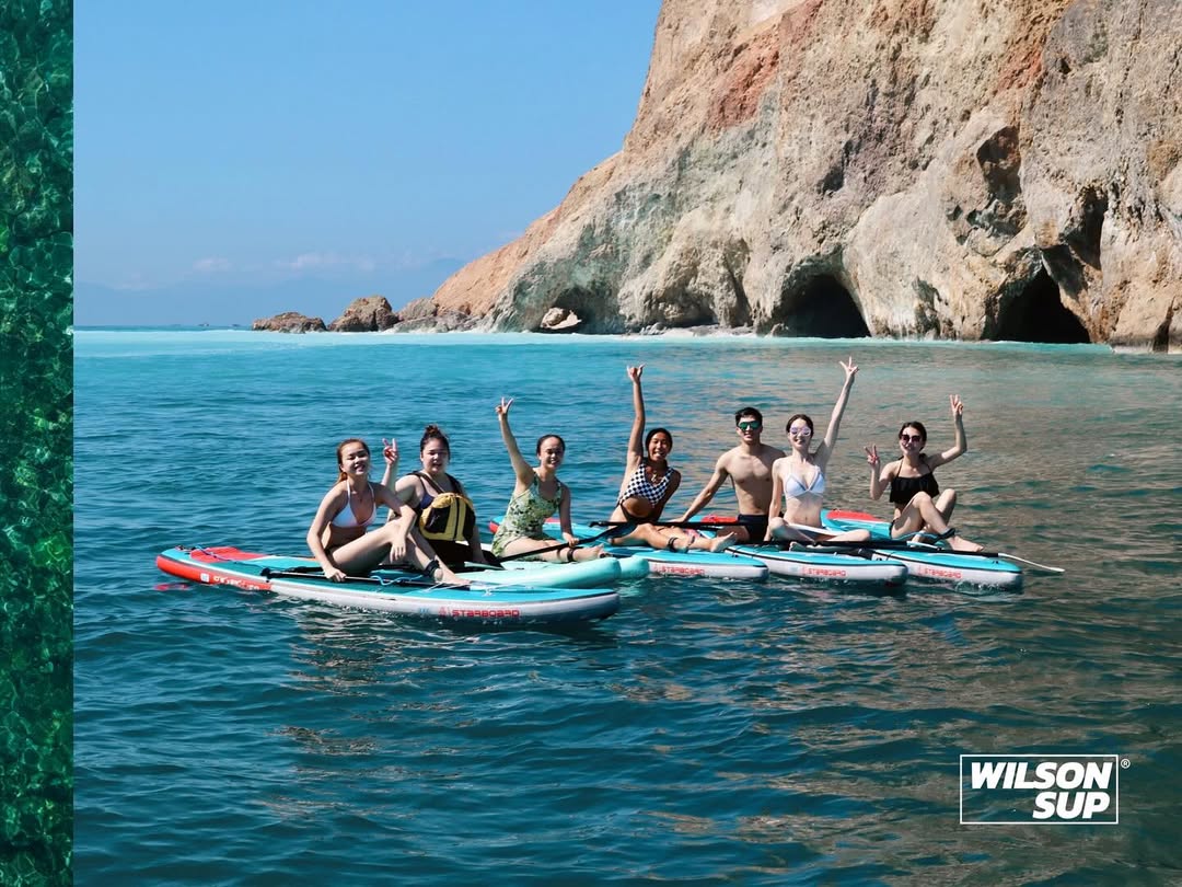 Taiwan SUP tour participants on paddleboards raising their hands in front of a sea cave